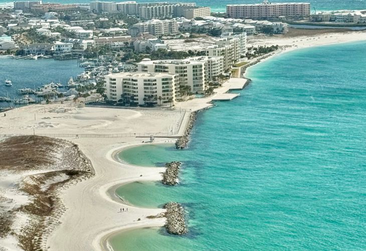 Aerial view of Destin, Florida real estate, with beachfront condos, a harbor, and the emerald green waters of the Gulf Coast.
