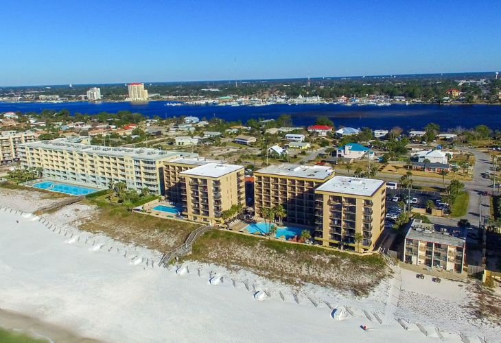 Destin real estate agent aerial view of Fort Walton Beach real estate on Okaloosa Island, showing beachfront condominium buildings with pools, the white-sand beach, and the Santa Rosa Sound in the background.