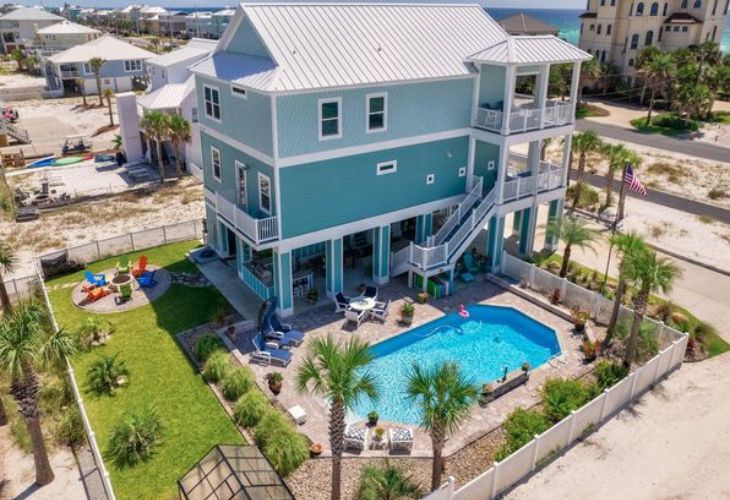 Aerial view of a luxury beach house for sale in Navarre Beach, FL, featuring a large private pool, multiple decks, and a lush green lawn.