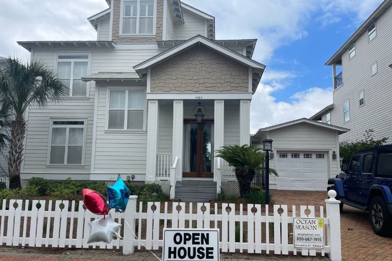 Destin real estate agent​showcase of a beautiful two-story coastal home in Destin, Florida with a white picket fence and an 'Open House' sign welcoming visitors.